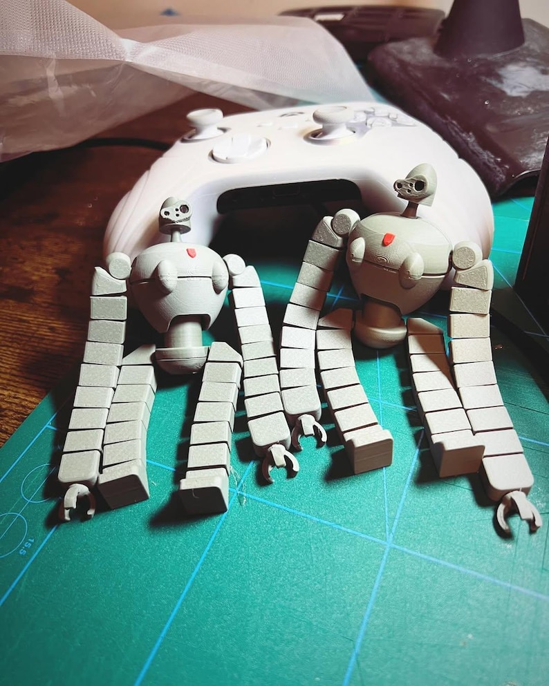 K&ouml;nnte beinhalten: Zwei graue, artikulierte Roboterfiguren mit mehreren segmentierten Gliedma&szlig;en. Die Roboter sind mit erhobenen Armen und gespreizten Beinen posiert. Die Figuren sind aus glattem, mattem Kunststoff.