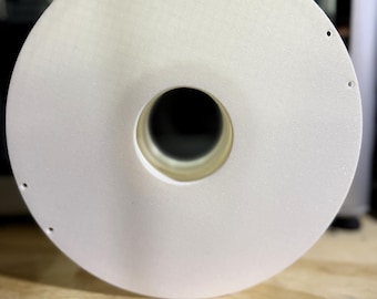 Peut inclure: Une bobine ronde en plastique blanche avec un trou au centre. La bobine est posée sur une surface en bois.