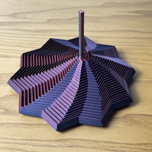 Puede incluir: Escultura geom&eacute;trica en forma de estrella con bordes en zigzag en capas. El degradado de color transita del morado oscuro a un tono rojo p&uacute;rpura. Una fina varilla texturizada se eleva desde el centro de la escultura.