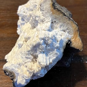 May include: A white, crystalline rock formation with a dark gray and brown outer layer. The rock has a rough, textured surface.