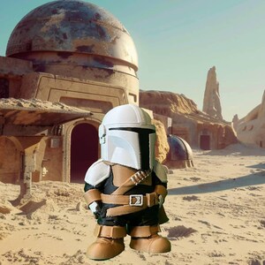 Handcrafted Mandalorian-inspired chibi figure stands in a sandy Tatooine-style desert with dome buildings, perfect for Star Wars fans, gift ideas, or collectors seeking unique handmade decor.