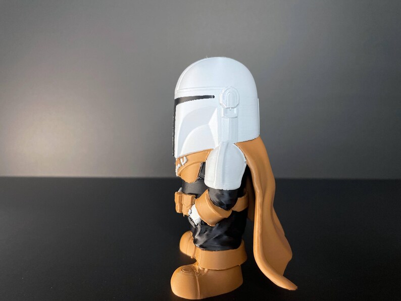 Cute, stylized Mandalorian figure in white and gold armor, set against a sandy sci-fi backdrop—an ideal collectible for fans, gift-givers, or lovers of pop culture decor.
