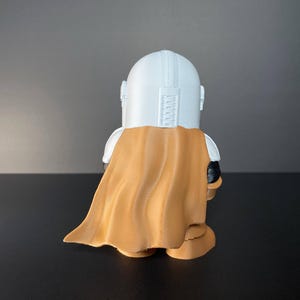 Handcrafted Mandalorian-inspired chibi figure in full armor, holding blaster, set against a desert landscape with iconic Tatooine structures—great for collectors, Star Wars enthusiasts, or as a unique gift idea.