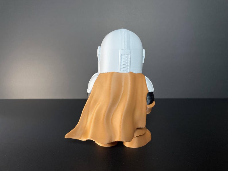 Handcrafted Mandalorian-inspired chibi figure in full armor, holding blaster, set against a desert landscape with iconic Tatooine structures—great for collectors, Star Wars enthusiasts, or as a unique gift idea.