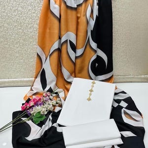 May include: A white salwar kameez set with gold embroidery and two matching fabric pieces. The set is paired with a patterned dupatta in orange, black, and white, and a bouquet of flowers.