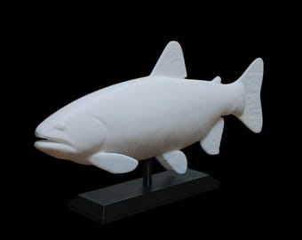 May include: A solid white fish sculpture featuring a smooth, matte finish, depicted in a swimming position. The fish is mounted on a simple, rectangular black base that provides a stable foundation for the display of this aquatic animal figure.