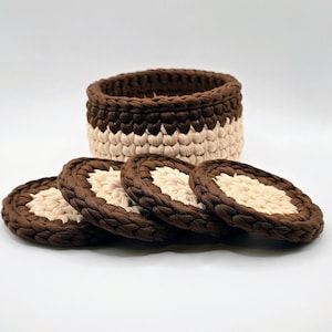 May include: A set of four round coasters and a matching basket. The coasters and basket are made of a thick, woven material in alternating bands of brown and beige. The basket is cylindrical.
