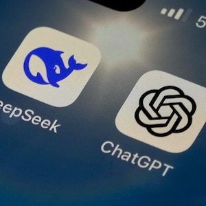 May include: A smartphone screen displaying two app icons. The left icon is blue and features a whale silhouette. The text "DeepSeek" is below the icon. The right icon is black and white and features a stylized knot design. The text "ChatGPT" is below the icon.