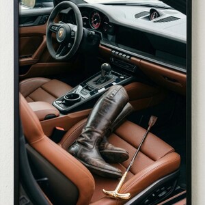 Puede incluir: Interior de un coche de lujo con asientos de cuero marr&oacute;n y un salpicadero negro. Un par de botas de montar de cuero marr&oacute;n y una fusta con mango dorado descansan en el asiento del conductor.