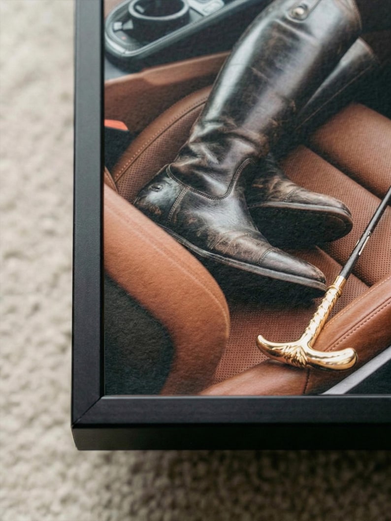 Puede incluir: Impresi&oacute;n enmarcada que muestra un par de botas de montar de cuero marr&oacute;n oscuro y desgastado sobre un asiento de coche de cuero marr&oacute;n. Tambi&eacute;n se ve un l&aacute;tigo de montar dorado. La imagen est&aacute; enmarcada en un marco negro.