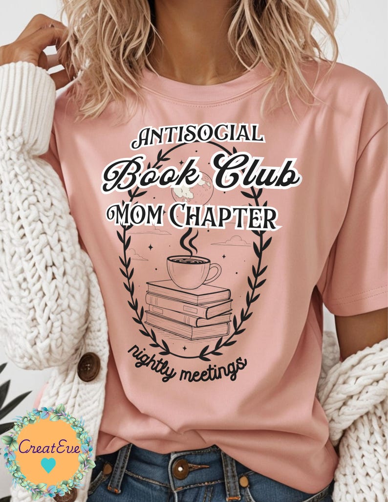 Op de afbeelding: Lichtroze t-shirt met de tekst "Antisocial Book Club Mom Chapter" in een decoratief lettertype. Het ontwerp bevat een stapel boeken, een koffiekopje en een krans. De zin "nightly meetings" is ook opgenomen.