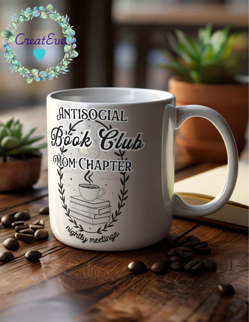 Op de afbeelding: Witte keramische mok met de tekst "ANTISOCIAL Book Club MOM CHAPTER nightly meetings" in zwart. Het ontwerp bevat een koffiekopje, boeken en een maan. De mok staat op een houten oppervlak met koffiebonen.