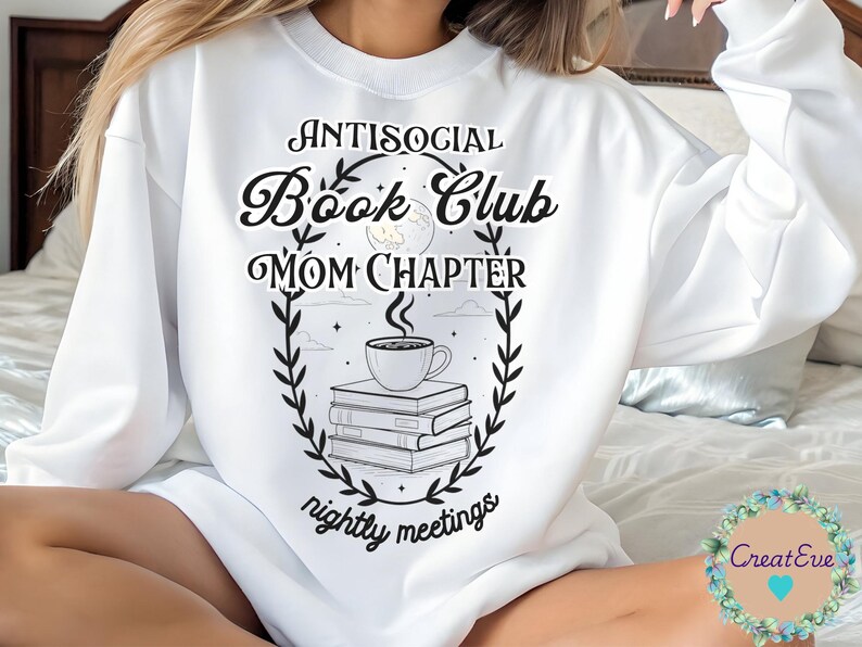 Op de afbeelding: Witte sweatshirt met de tekst "Antisocial Book Club Mom Chapter nightly meetings" in zwarte, decoratieve letters. Een afbeelding van een koffiekopje op boeken staat in het midden, omlijst door een krans.