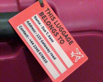 May include: A coral luggage tag with the text "THIS LUGGAGE BELONGS TO" and the owner's details. The tag includes a white airplane graphic. It is attached to a pink suitcase. The tag's contact number is displayed.