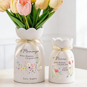 Peut inclure: Deux vases en céramique blanche avec des motifs floraux et des rubans dorés. L'un des vases contient un bouquet de tulipes jaunes, roses et crème. Le texte sur les vases se lit : "Si les mamans étaient des fleurs, je vous choisirais. Love, Sophia" et "Si les Nanas étaient des fleurs, je vous choisirais. Love Sophia."