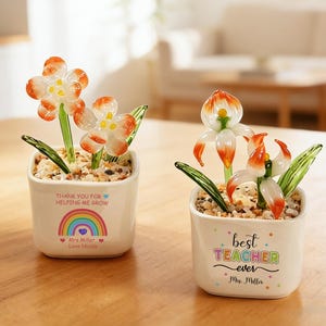 May include: Two square white ceramic planters filled with small pebbles and glass flowers. The left planter features a rainbow graphic and text reading THANK YOU FOR HELPING ME GROW Mrs Miller Love Nicole. The right planter says best TEACHER ever Mrs. Miller.