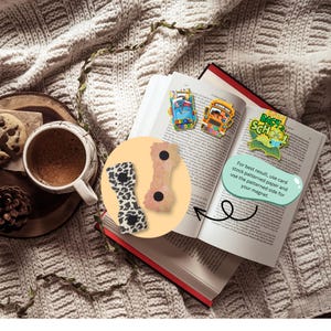 May include: An open book with red edges displays colorful "Back to School" magnets and a text bubble. Two decorative magnets are shown in a circle, one with a black and white pattern and the other with a pinkish hue. A cup of coffee and cookies are on a wooden tray.