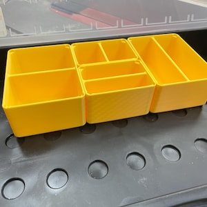 May include: Four yellow plastic storage containers with dividers. The containers are sitting in a black tray with circular holes.