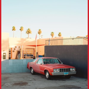 May include: A vintage, light pink car parked in a car park with a grey concrete wall and a black fence in the background. The car has a blue number plate with the text "792-491".