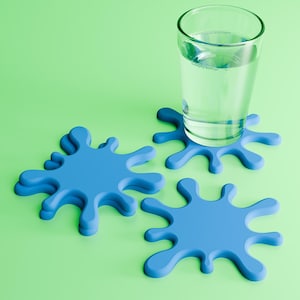 Puede incluir: Un vaso de agua transparente descansa sobre un posavasos azul en forma de salpicadura. También se ven dos posavasos azules adicionales. Los posavasos están sobre una superficie verde claro.