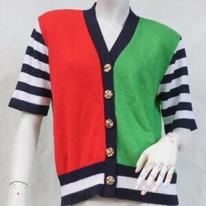 May include: A short-sleeved cardigan with a red, green, and blue color block design. The cardigan has a V-neck and gold buttons.