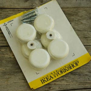 May include: A pack of six white plastic knobs with screws, labelled "IKEA WORKSHOP".