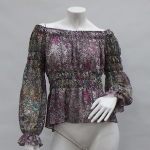 May include: Off-the-shoulder blouse with long sleeves. The sheer fabric features a floral pattern in shades of purple, green, and white. The blouse has a gathered waist and elasticated cuffs. The neckline is also elasticated.