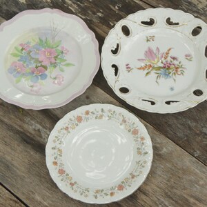 May include: Three white ceramic plates with floral designs. The plates have scalloped edges and are decorated with pink, blue, and yellow flowers.