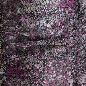 May include: Close-up of a fabric with a floral pattern. The design features small, tightly packed flowers in shades of pink, white, and gray against a black background. The fabric appears to be slightly sheer, with a gathered or ruched texture.