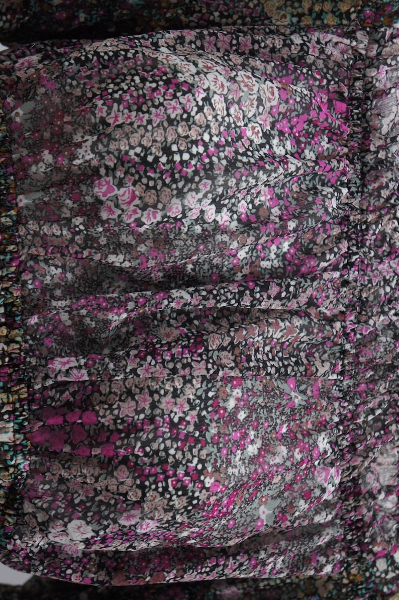 May include: Close-up of a fabric with a floral pattern. The design features small, tightly packed flowers in shades of pink, white, and gray against a black background. The fabric appears to be slightly sheer, with a gathered or ruched texture.