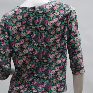 Puede incluir: Una blusa de estampado floral negro, verde y rosa con cierre de botones en la espalda.