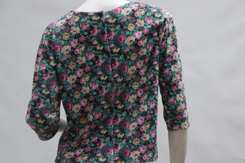 Puede incluir: Una blusa de estampado floral negro, verde y rosa con cierre de botones en la espalda.