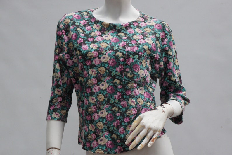 Puede incluir: Una camisa de manga 3/4 de color negro con estampado floral y un peque&ntilde;o bolsillo en el lado izquierdo.
