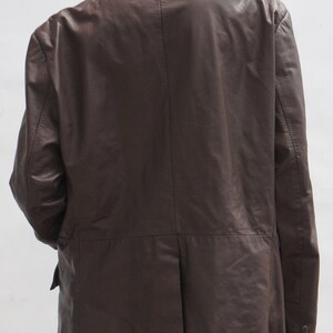 May include: A dark brown leather blazer with a classic design. The jacket features a notched lapel, a two-button closure, and a single vent in the back. The sleeves have buttoned cuffs. The blazer is shown from the back.