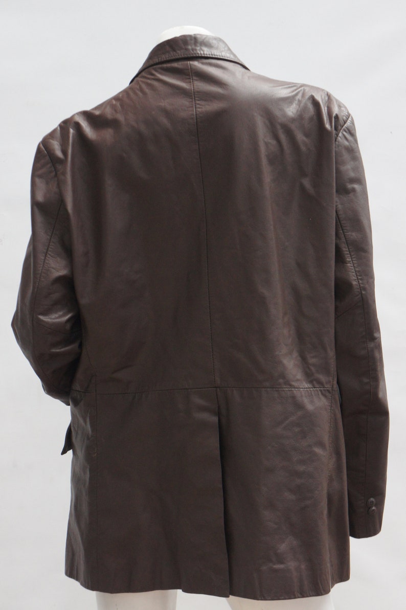 May include: A dark brown leather blazer with a classic design. The jacket features a notched lapel, a two-button closure, and a single vent in the back. The sleeves have buttoned cuffs. The blazer is shown from the back.