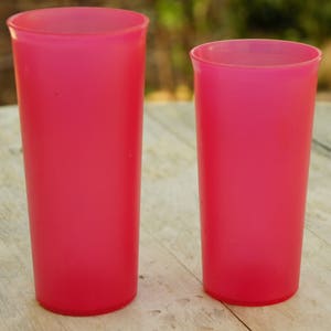 May include: Two pink plastic cups, one taller than the other, on a wooden surface.