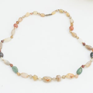 May include: A necklace made of various colored stones, including brown, green, and white. The stones are oval-shaped and strung together on a gold chain.