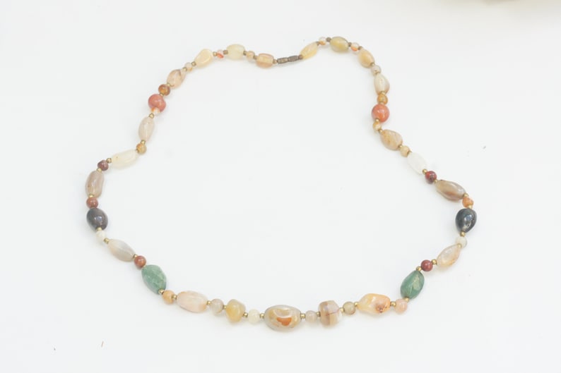 May include: A necklace made of various colored stones, including brown, green, and white. The stones are oval-shaped and strung together on a gold chain.
