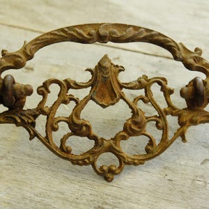 May include: Ornate antique drawer pull with a decorative, scrolled design. The pull is made of metal and has a rustic, aged finish.
