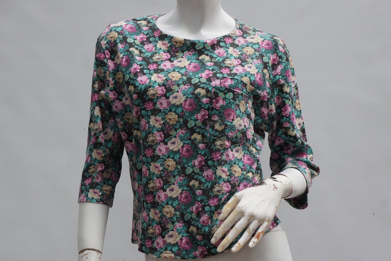 Puede incluir: Una camisa de manga 3/4 de color negro con estampado floral y un peque&ntilde;o bolsillo en el lado izquierdo.