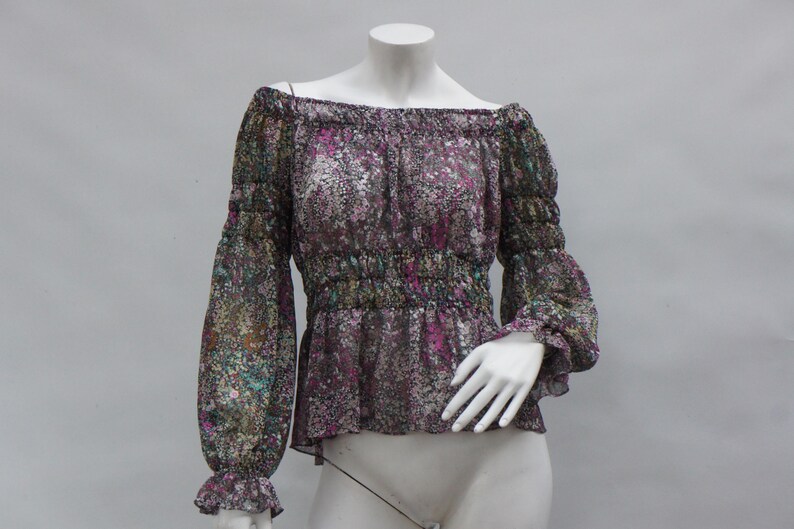May include: Off-the-shoulder blouse with long sleeves. The sheer fabric features a floral pattern in shades of purple, green, and white. The blouse has a gathered waist and elasticated cuffs. The neckline is also elasticated.