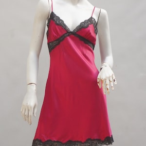 May include: A red satin slip dress with black lace trim. The dress has a V-neckline and adjustable straps.