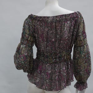 May include: A sheer, off-the-shoulder blouse with long sleeves. The blouse features a floral pattern in shades of purple, green, and yellow. The sleeves are gathered at the wrists, and the waist is cinched with elastic. The blouse has a peplum hem.
