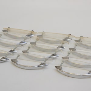 May include: A collection of vintage cabinet handles. Each handle features a curved, polished silver metal pull with a clear, curved plastic backing. The handles are arranged in rows against a white background, suggesting a hardware or home decor theme.