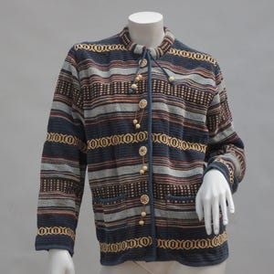 May include: A long-sleeved, button-down jacket with a striped pattern in navy blue, grey, and brown. The jacket features decorative trim and wooden buttons. The garment is displayed on a mannequin.