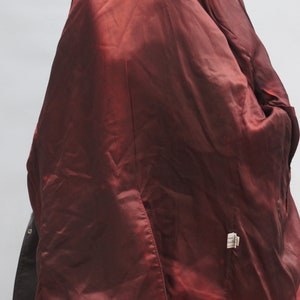 May include: A dark brown blazer with a deep red satin lining. The interior of the jacket is visible, showcasing the rich color and texture of the lining. The blazer is buttoned and appears to be made of leather or a similar material.