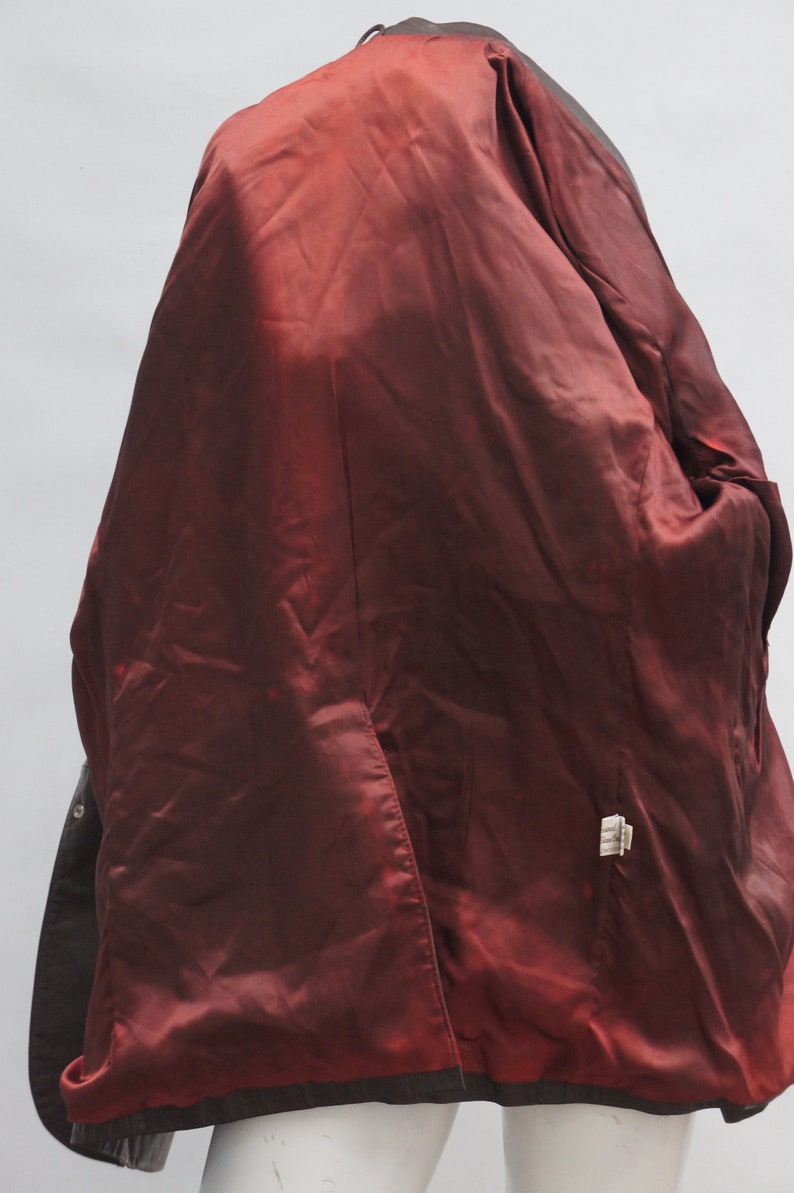 May include: A dark brown blazer with a deep red satin lining. The interior of the jacket is visible, showcasing the rich color and texture of the lining. The blazer is buttoned and appears to be made of leather or a similar material.
