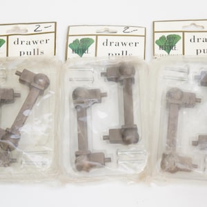 May include: Three packages of vintage drawer pulls. Each package contains two brown metal pulls and screws, displayed on a cream-colored card with the text "drawer pulls". The cards have a green leaf logo.