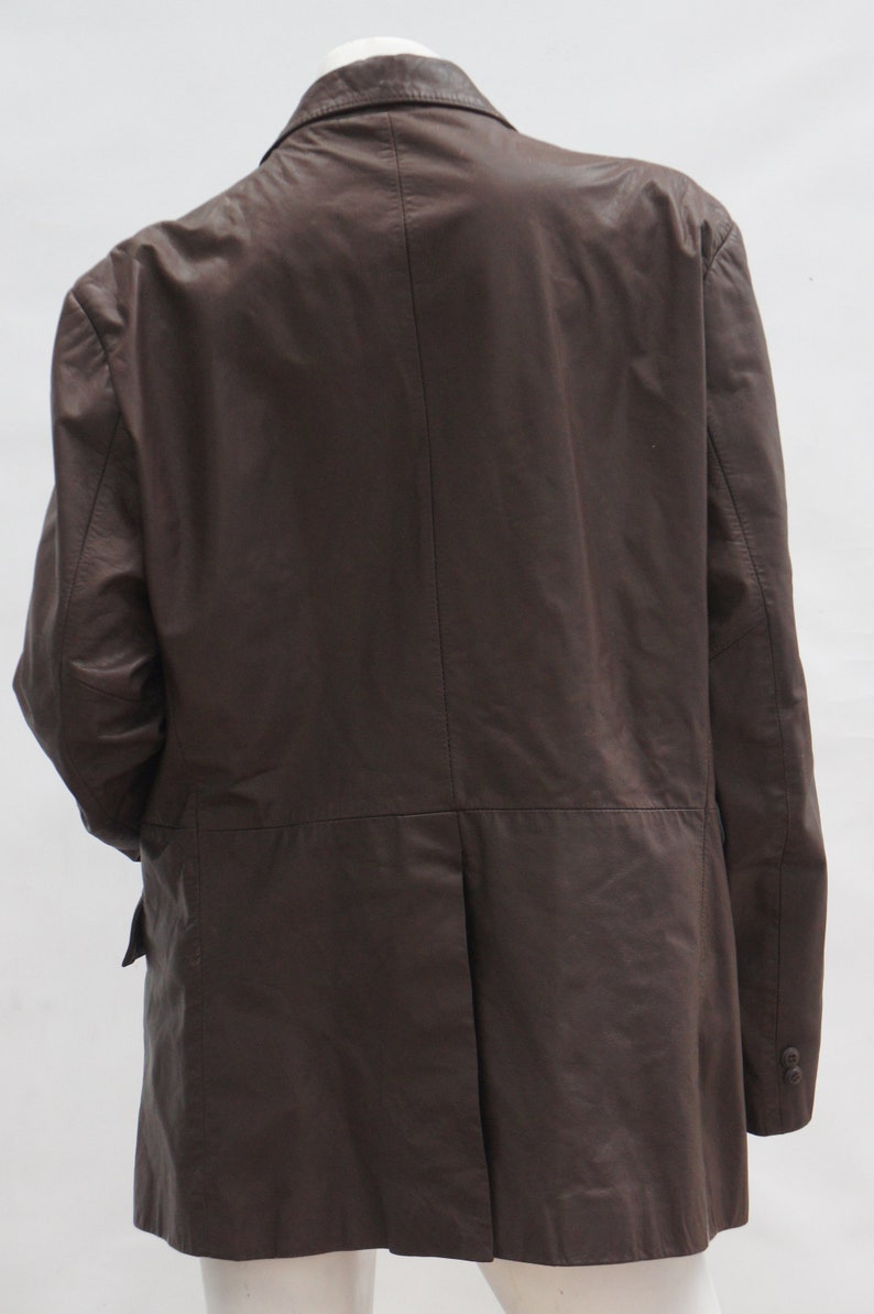 May include: A brown leather blazer with a classic design. The jacket features a notched lapel, two-button closure, and a single vent in the back. The sleeves have buttoned cuffs. The blazer is displayed on a mannequin.