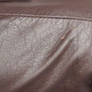 May include: Close-up of a brown leather jacket. The leather has a textured, wrinkled appearance with visible stitching along the seams. The color is a rich, dark brown.